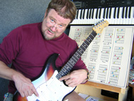 Photograph of Scotty pointing out on his guitar how music theory is applied to the guitar fretboard.